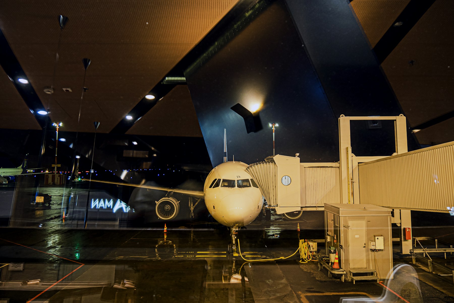An airliner at the gate at dusk, seen through a dark terminal with warm lights